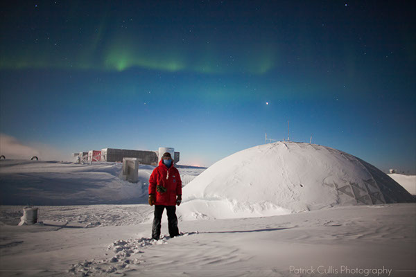 Patrick Cullis posing in front of the Dome and Elevated Stations at the South Pole, Antarctica.
